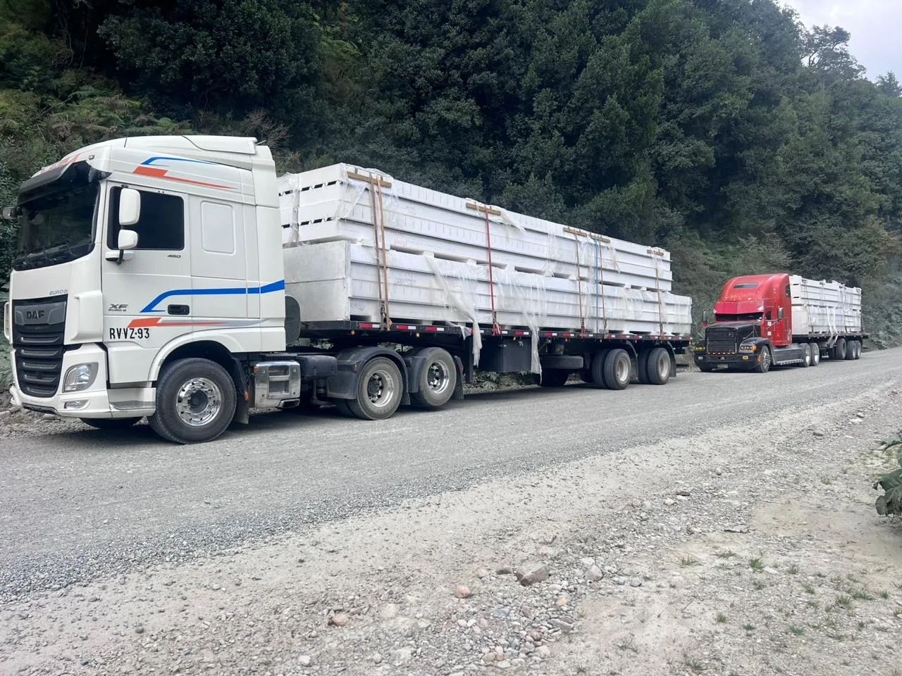 Dos camiones blancos cargados en una carretera rodeada de árboles